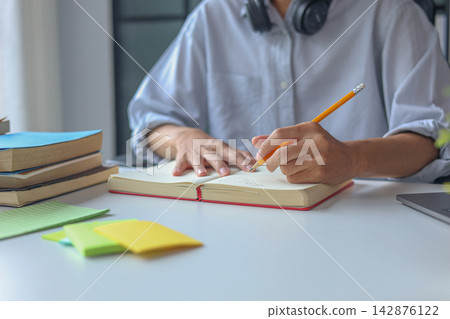 Close-up young man writing in the notebook while studying on the table with laptop and books. Close-up young man writing in the notebook while studying on the table with laptop and books. 142876122
