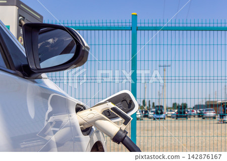 Electric vehicle charging at outdoor station with turquoise fence Electric vehicle charging at outdoor station with turquoise fence 142876167
