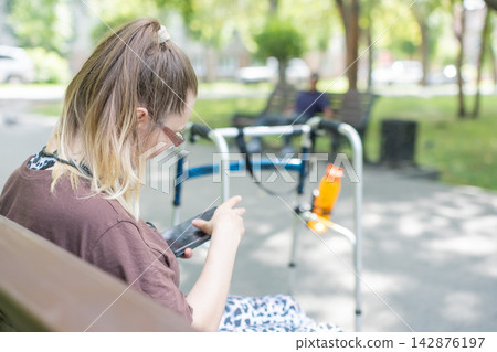 A Caucasian woman with cerebral palsy sits on a park bench. A Caucasian woman with cerebral palsy sits on a park bench. 142876197