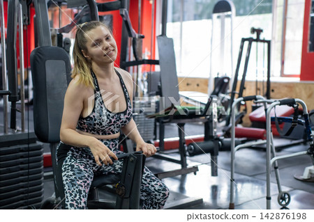 A woman with cerebral palsy exercises on a machine in a gym. A woman with cerebral palsy exercises on a machine in a gym. 142876198