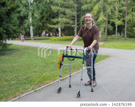 A young woman with cerebral palsy walks in a park with a walker. A young woman with cerebral palsy walks in a park with a walker. 142876199
