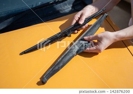 A woman replaces old windshield wipers with new ones on a car. 142876200