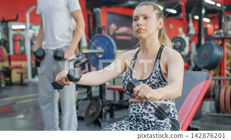 A Caucasian woman with cerebral palsy exercises with dumbbells in a gym. A Caucasian woman with cerebral palsy exercises with dumbbells in a gym. 142876201
