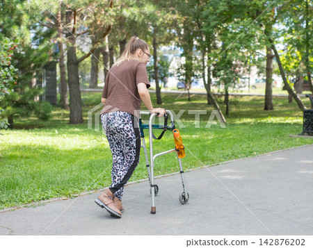 A young woman with cerebral palsy walks in a park with a walker. 142876202