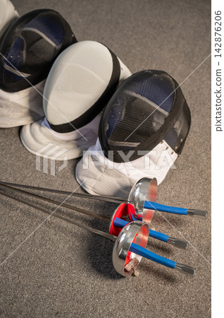 Fencing equipment. Swords and masks on the gray floor. Fencing equipment. Swords and masks on the gray floor. 142876206