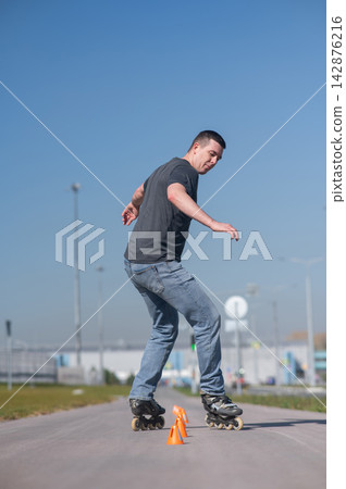 A Caucasian man rollerblades around the slalom course. A Caucasian man rollerblades around the slalom course. 142876216