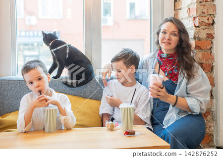 A Caucasian woman, her two sons, and a cat are having lunch at a cafe. Pet friendly. 142876252