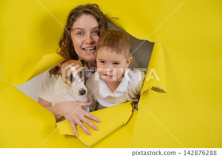 Caucasian little boy, his mother and Jack Russell Terrier dog tearing yellow paper background. Caucasian little boy, his mother and Jack Russell Terrier dog tearing yellow paper background. 142876288