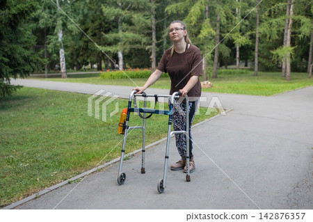 A young woman with cerebral palsy walks in a park with a walker. A young woman with cerebral palsy walks in a park with a walker. 142876357