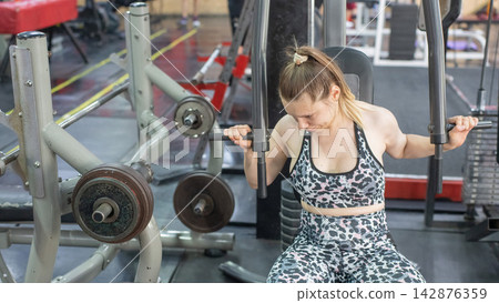 A woman with cerebral palsy exercises on a machine in a gym. A woman with cerebral palsy exercises on a machine in a gym. 142876359