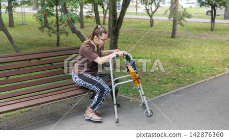 A Caucasian woman with cerebral palsy sits on a park bench. A Caucasian woman with cerebral palsy sits on a park bench. 142876360