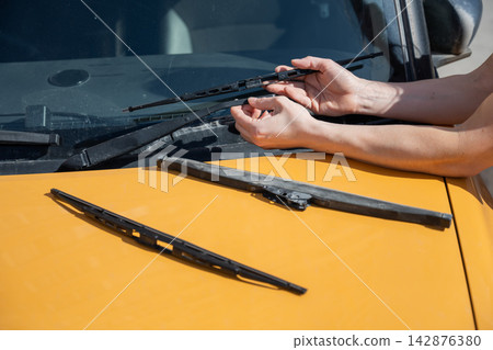 A woman replaces old windshield wipers with new ones on a car. A woman replaces old windshield wipers with new ones on a car. 142876380