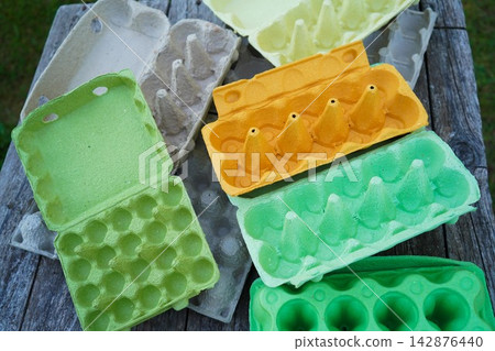 Molded fiber egg crates in green yellow and grey on rustic surface backdrop 142876440