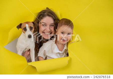 Caucasian little boy, his mother and Jack Russell Terrier dog tearing yellow paper background. Caucasian little boy, his mother and Jack Russell Terrier dog tearing yellow paper background. 142876518