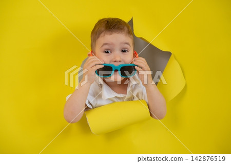 Caucasian little boy in sunglasses tearing yellow paper background. Caucasian little boy in sunglasses tearing yellow paper background. 142876519