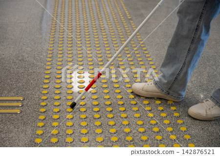 A blind woman walks on tactile paving. Close-up of her feet and a walking stick. A blind woman walks on tactile paving. Close-up of her feet and a walking stick. 142876521