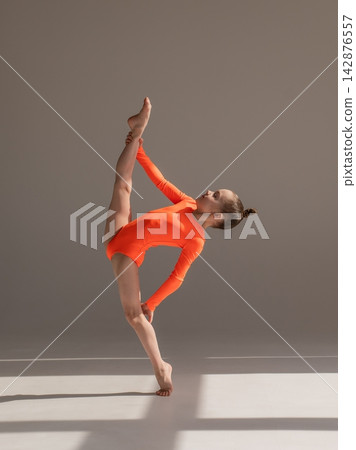 A little Caucasian girl gymnast in an orange leotard demonstrates her skills on a white background. A little Caucasian girl gymnast in an orange leotard demonstrates her skills on a white background. 142876557