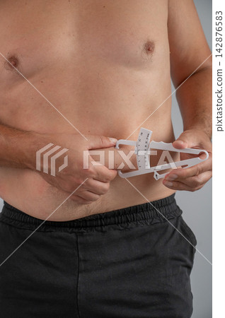 A man measures the amount of subcutaneous fat on his stomach using a caliper. A man measures the amount of subcutaneous fat on his stomach using a caliper. 142876583