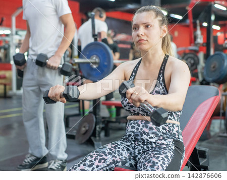 A Caucasian woman with cerebral palsy exercises with dumbbells in a gym. 142876606