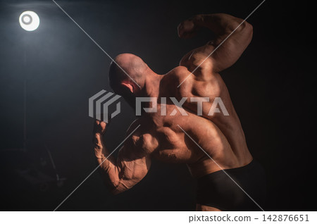 A male bodybuilder poses in shorts, showing off his back muscles. A male bodybuilder poses in shorts, showing off his back muscles. 142876651