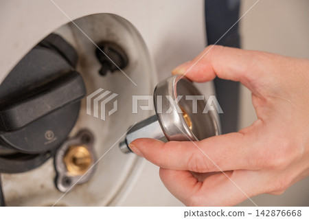 A woman installs an adapter on a gas tank in a car. 142876668