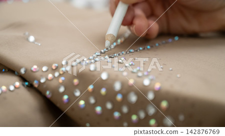 A woman decorates her gymnastics costume with rhinestones. Rhythmic gymnastics. A woman decorates her gymnastics costume with rhinestones. Rhythmic gymnastics. 142876769