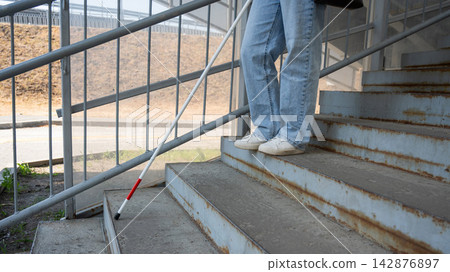A blind woman descends a staircase. Close-up of her feet and a tactile stick. A blind woman descends a staircase. Close-up of her feet and a tactile stick. 142876897