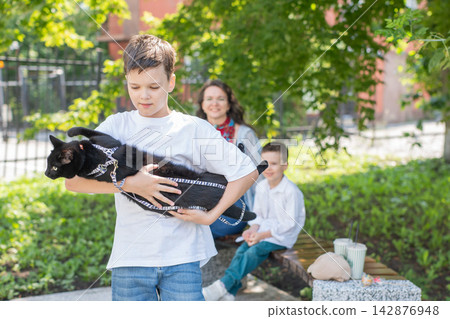 A woman and her two sons are walking a cat. A woman and her two sons are walking a cat. 142876948
