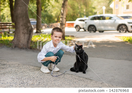 A Caucasian boy walks with a cat on a leash outdoors. A Caucasian boy walks with a cat on a leash outdoors. 142876968