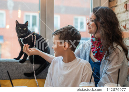 A Caucasian woman, her son, and her cat are having lunch at a cafe. Pet friendly. A Caucasian woman, her son, and her cat are having lunch at a cafe. Pet friendly. 142876977