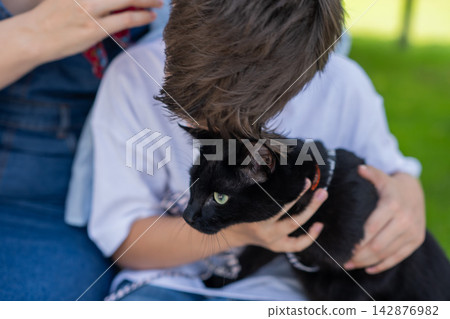 A Caucasian woman and her son walk their cat on a leash. A Caucasian woman and her son walk their cat on a leash. 142876982
