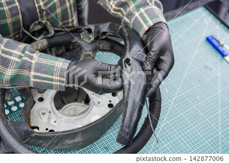 The mechanic changes the cover on the car steering wheel. The mechanic changes the cover on the car steering wheel. 142877006