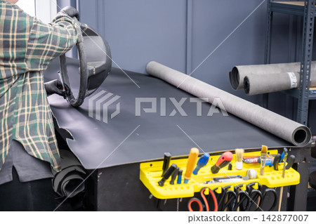 A seamstress in a workshop makes a new leather cover for a car steering wheel. A seamstress in a workshop makes a new leather cover for a car steering wheel. 142877007