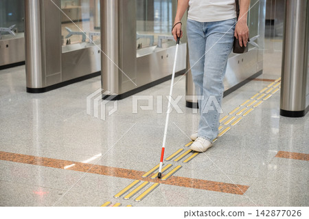 A blind woman passes through a turnstile in the subway. A blind woman passes through a turnstile in the subway. 142877026