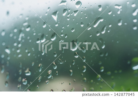 A quiet rainy season background image featuring raindrops on a windowpane and blurred greenery. A quiet rainy season background image featuring raindrops on a windowpane and blurred greenery. 142877045