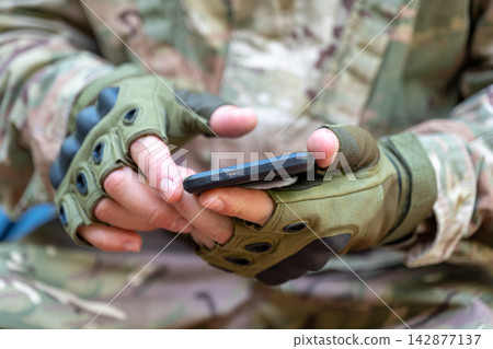 Gloved soldier hands holding smartphone in camouflage uniform closeup Gloved soldier hands holding smartphone in camouflage uniform closeup 142877137