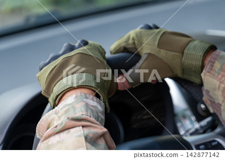 Camouflaged gloved hands gripping steering wheel inside vehicle cabin Camouflaged gloved hands gripping steering wheel inside vehicle cabin 142877142