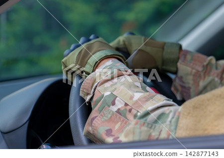 Camouflaged hands gripping steering wheel inside moving vehicle close up Camouflaged hands gripping steering wheel inside moving vehicle close up 142877143