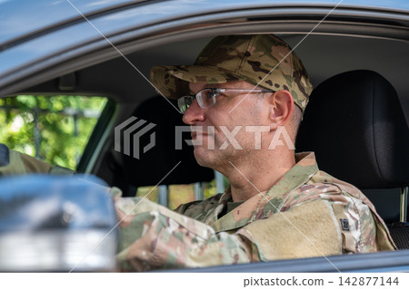 Focused military driver sitting inside vehicle wearing camouflage uniform Focused military driver sitting inside vehicle wearing camouflage uniform 142877144