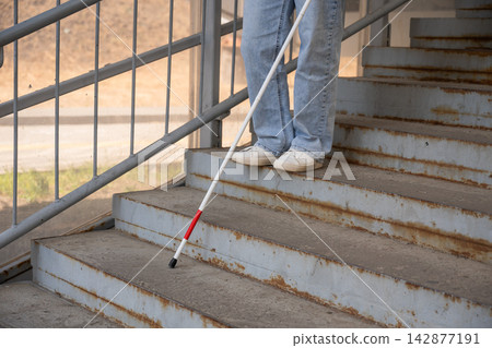 A blind woman descends a staircase. Close-up of her feet and a tactile stick. A blind woman descends a staircase. Close-up of her feet and a tactile stick. 142877191