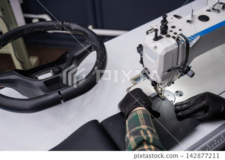 A seamstress in a workshop makes a new leather cover for a car steering wheel. A seamstress in a workshop makes a new leather cover for a car steering wheel. 142877211