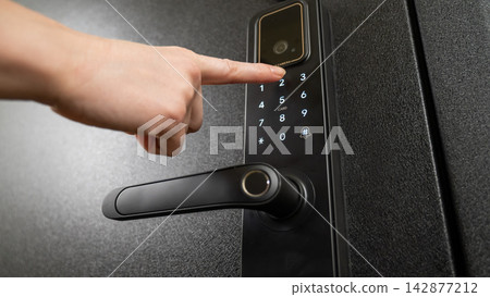 A woman opens a modern smart door lock with a digital keypad using a code. A woman opens a modern smart door lock with a digital keypad using a code. 142877212