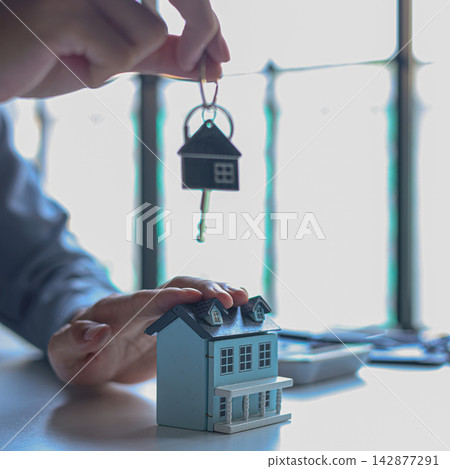 Hand holding key with house-shaped keychain. Concept for buying, selling, renting or leasing a new home. 142877291