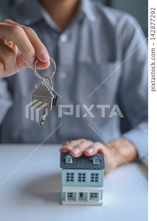 Hand holding key with house-shaped keychain. Concept for buying, selling, renting or leasing a new home. Hand holding key with house-shaped keychain. Concept for buying, selling, renting or leasing a new home. 142877292