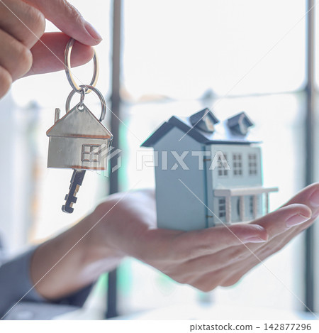 Real estate agent handing over the key with small house model for property purchase or rental. 142877296