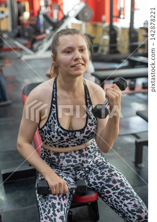 A Caucasian woman with cerebral palsy exercises with dumbbells in a gym. A Caucasian woman with cerebral palsy exercises with dumbbells in a gym. 142878221