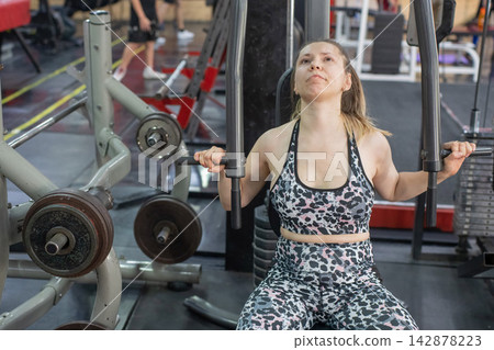 A woman with cerebral palsy exercises on a machine in a gym. A woman with cerebral palsy exercises on a machine in a gym. 142878223