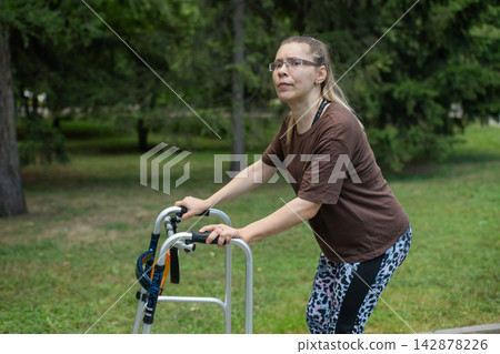 A young woman with cerebral palsy walks in a park with a walker. A young woman with cerebral palsy walks in a park with a walker. 142878226
