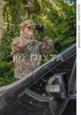 Military scout conducts secret surveillance near a vehicle while gathering information for a special operation. Military scout conducts secret surveillance near a vehicle while gathering information for a special operation. 142878343