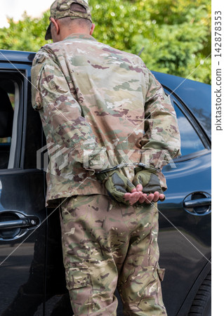 Detained man in military camouflage stands handcuffed beside a vehicle after a failed covert intelligence operation. Detained man in military camouflage stands handcuffed beside a vehicle after a failed covert intelligence operation. 142878353